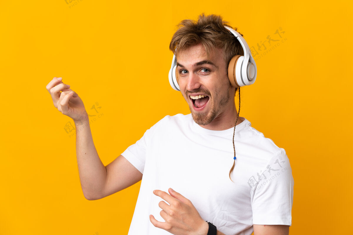 男人年轻英俊的金发男子孤立在黄色背景下听音乐 做吉他手势听力成人帅哥