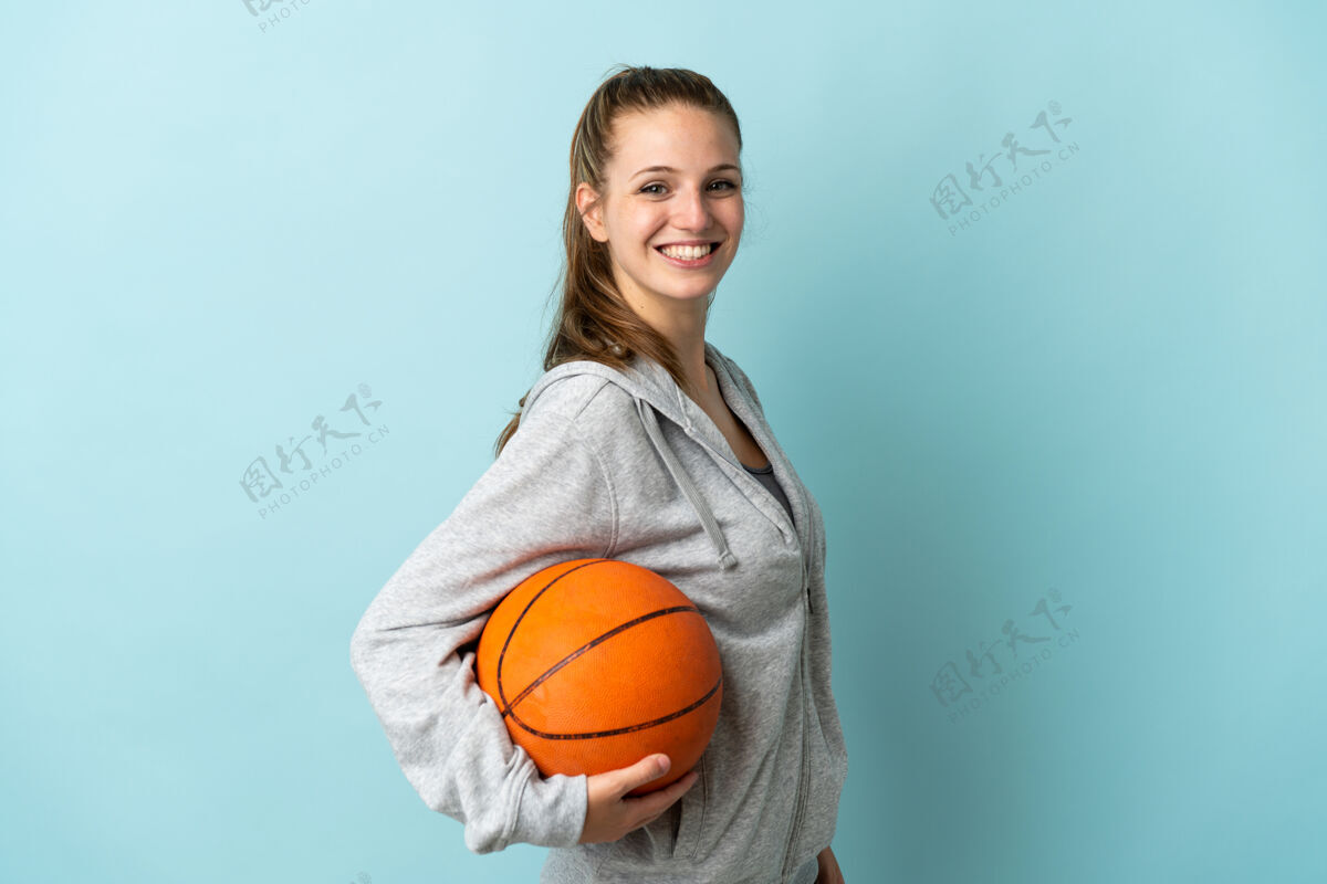 运动装年轻的白人女子在蓝色背景下打篮球积极年轻运动员