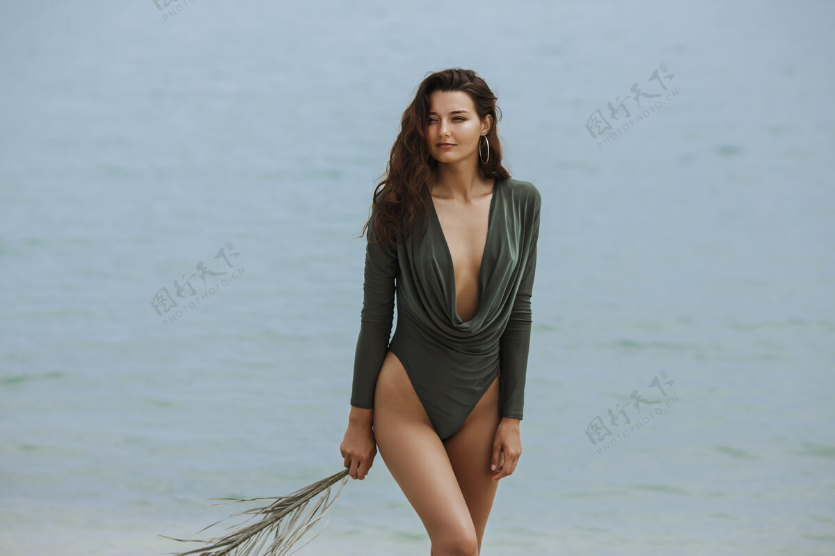 泰国一个穿着时尚泳装 手持棕榈叶 站在海边的女模特热热带年轻