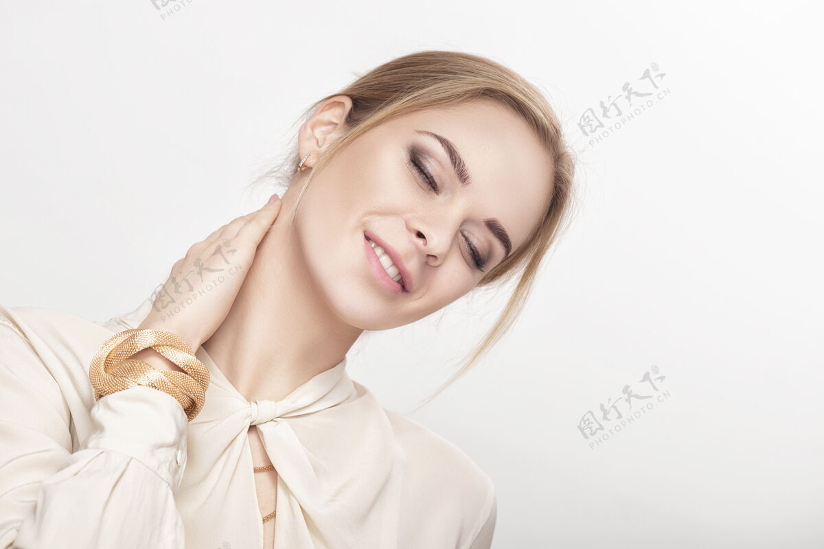 一个一位穿着白衬衫的年轻性感金发美女微笑着看着她相机性感金发女郎封闭背景皮肤护理