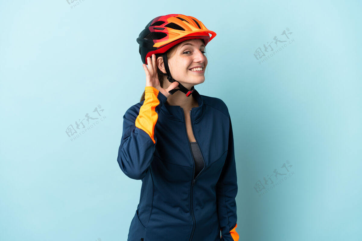 运动一个骑自行车的年轻女子被隔离在蓝色背景下 用手捂着耳朵听东西听骑车人表情