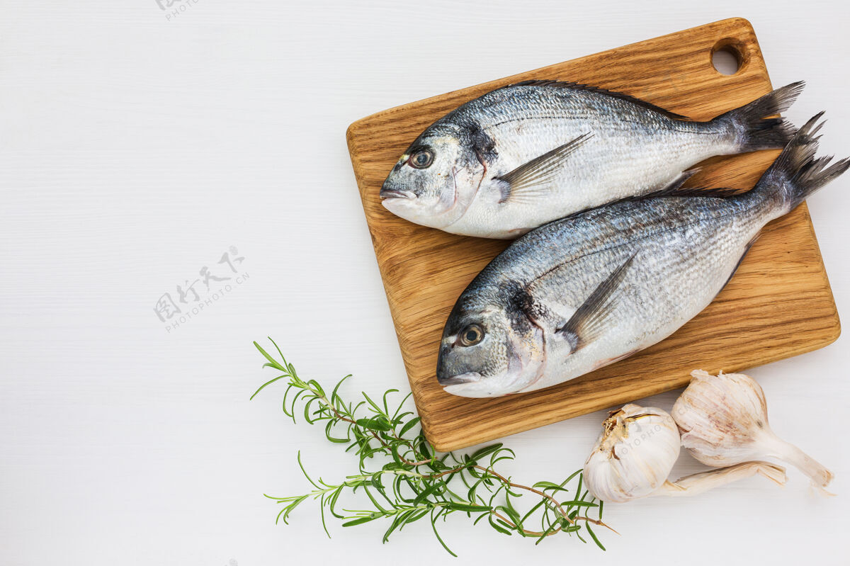 大蒜新鲜的多拉多鱼放在木制的切肉板上 白色的大蒜和迷迭香桌面查看 复制晚餐配料蛋白质