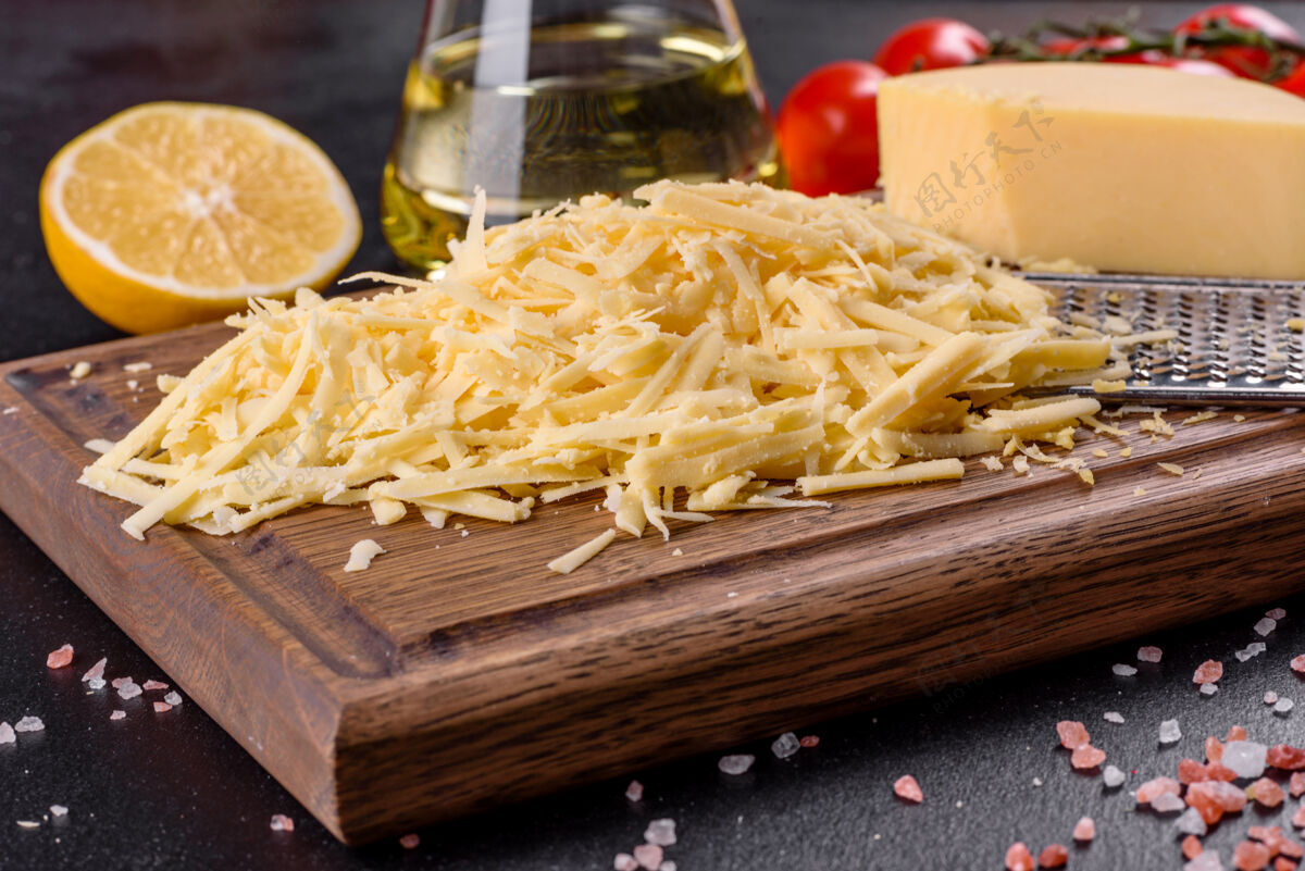 烹饪新鲜的硬奶酪磨碎在一个大的磨碎机在一个黑暗的混凝土背景木制砧板切丝堆开胃菜