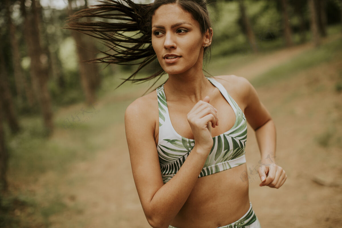 长跑在森林小道上跑步的年轻漂亮的健身女士跑步私人教练小径
