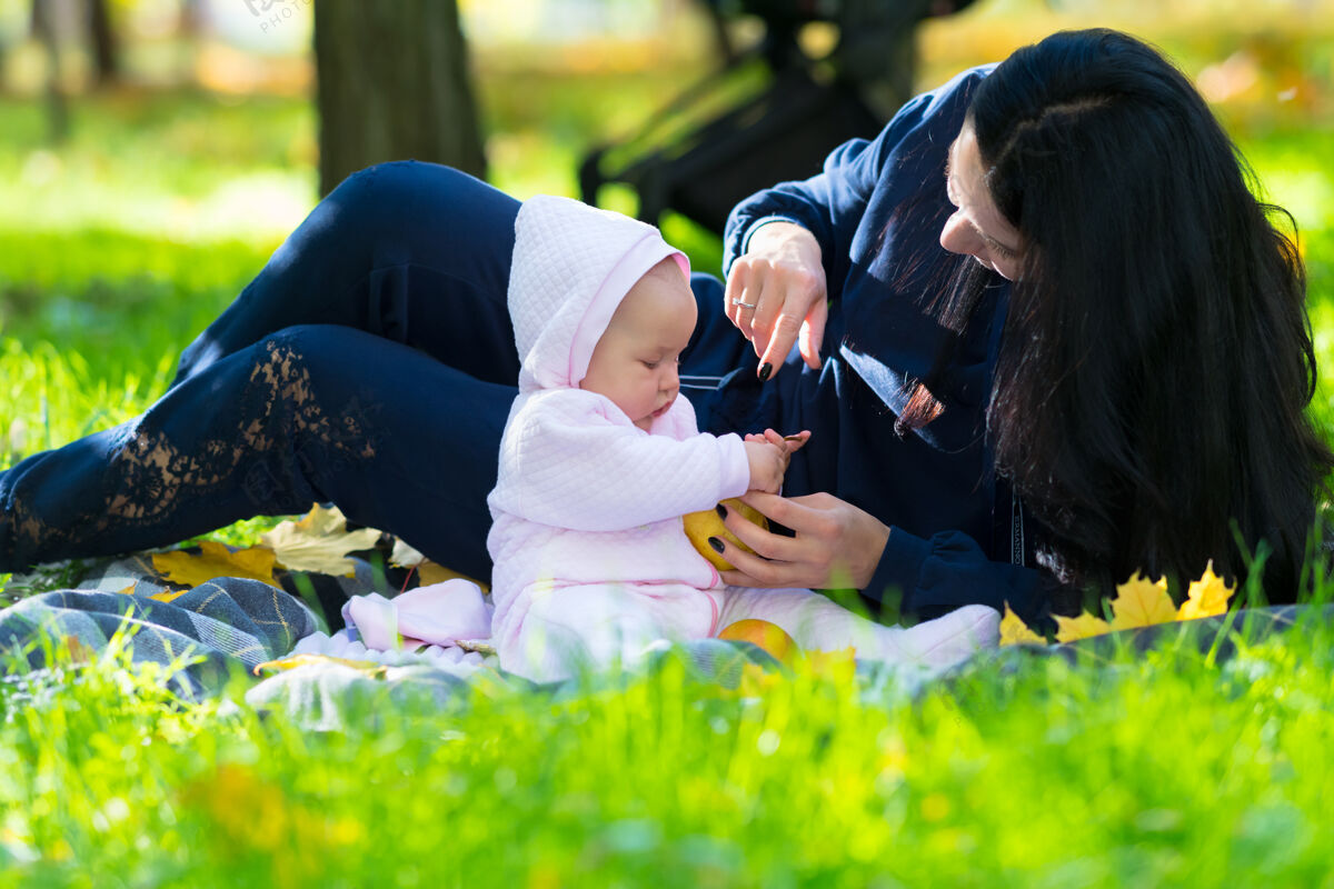 女儿秋天 年轻的妈妈和一个穿着粉色套装的女婴在花园或公园里玩耍女人多彩坐着