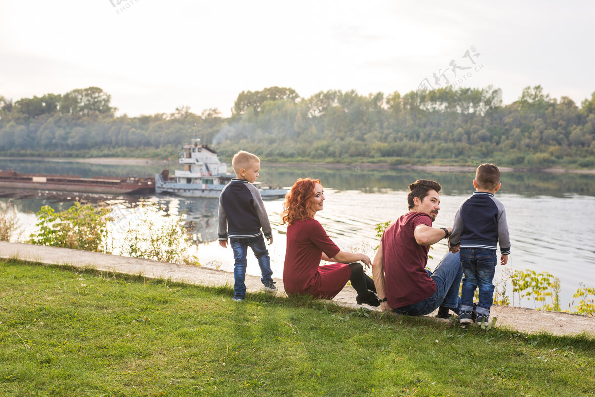 儿子亲子 童年和自然的概念-一家人坐在绿色的土地上 看着小家庭男性爱