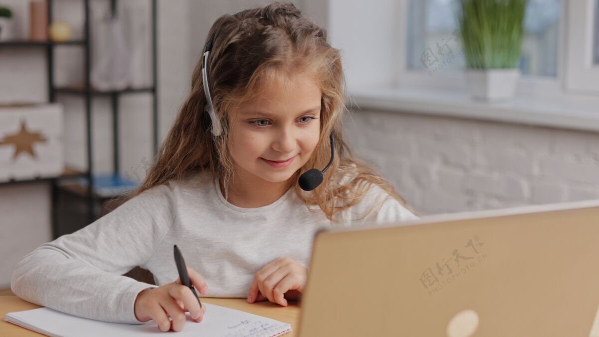 室内女生在耳机里有在线课 视频通话用老师可爱小学女生在家用笔记本电脑学习学生在线家庭作业