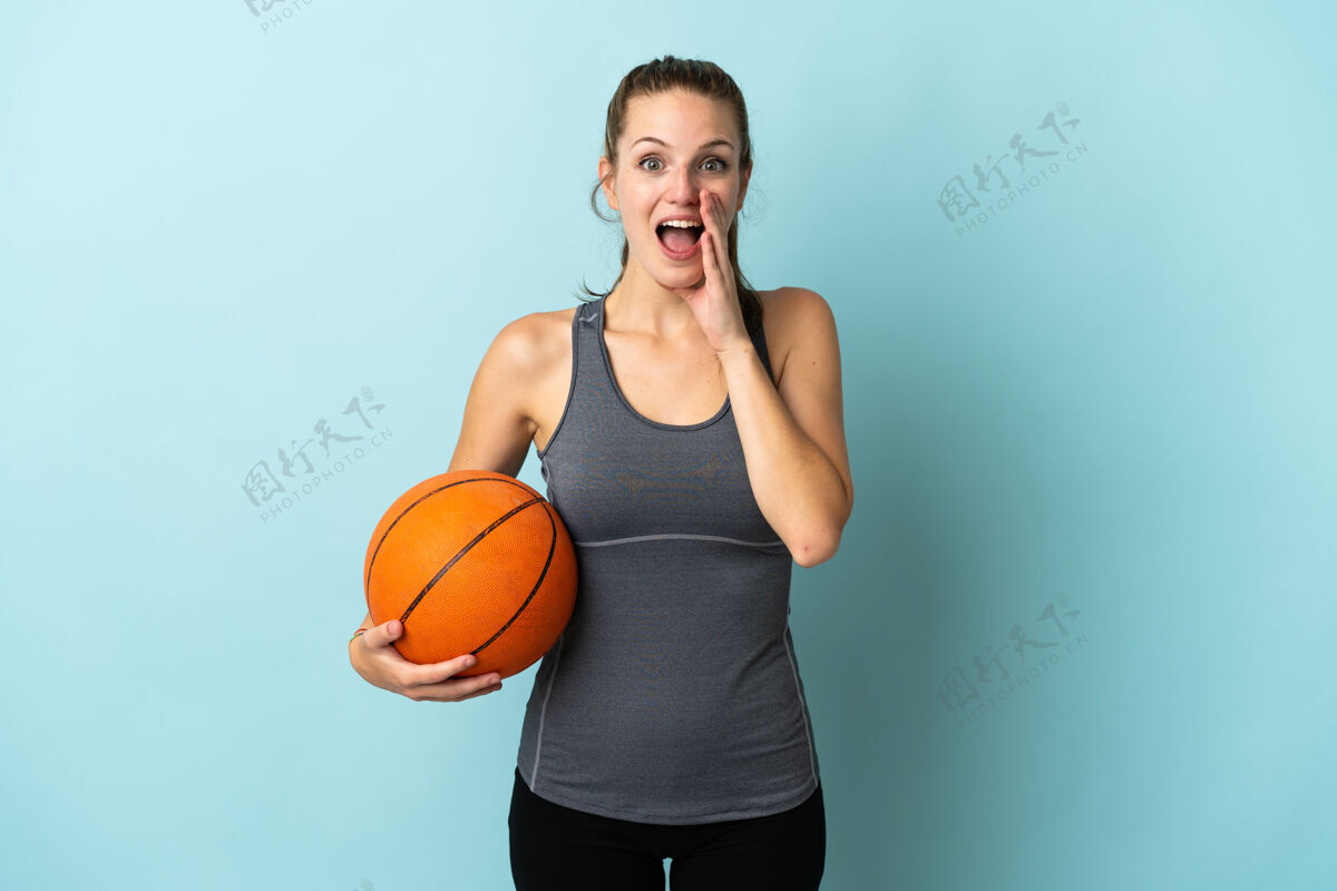 惊喜在蓝色背景上打篮球的年轻女子 脸上露出惊讶和震惊的表情哇成人身体