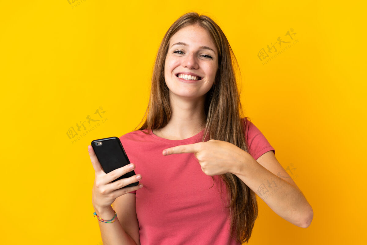 通话年轻女子用手机隔离在黄色的背景下指着它女人女孩电话