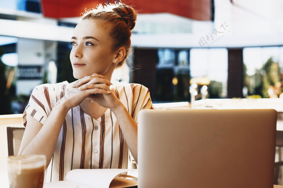肖像一位迷人的年轻女子的画像 她有着红发和雀斑 手放在手上 一边看着别处 一边在外面喝咖啡通信互联网社交媒体