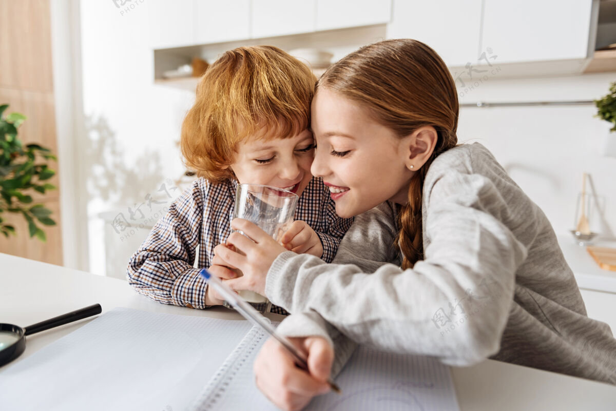 学习美味可口营养丰富美丽幽默的年轻女孩在做家庭作业的时候 一边喝着弟弟的牛奶一边逗他数学世代游戏