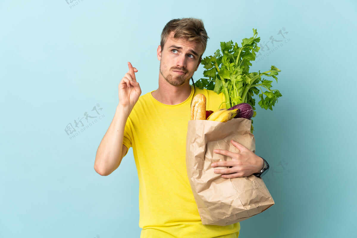 青年金发碧眼的人拿着一袋外卖食物 手指交叉着放在蓝色的桌子上 祝你好运农场蔬菜膳食