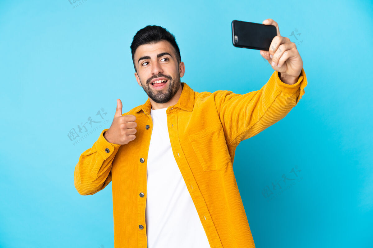 说话一个白人男子在孤立的蓝色背景下用手机自拍男性成人好