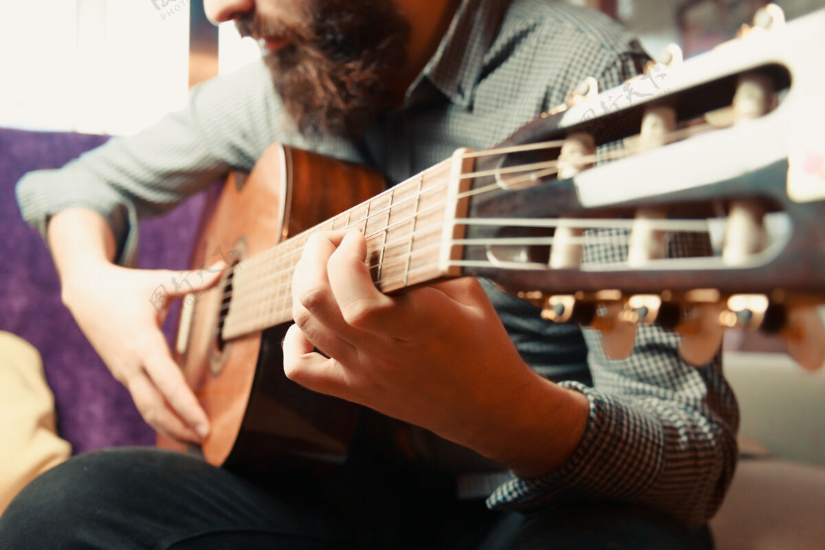 人在一个明亮的日子里 一个留着胡子的男人弹奏西班牙吉他的手的特写镜头男性现代时髦