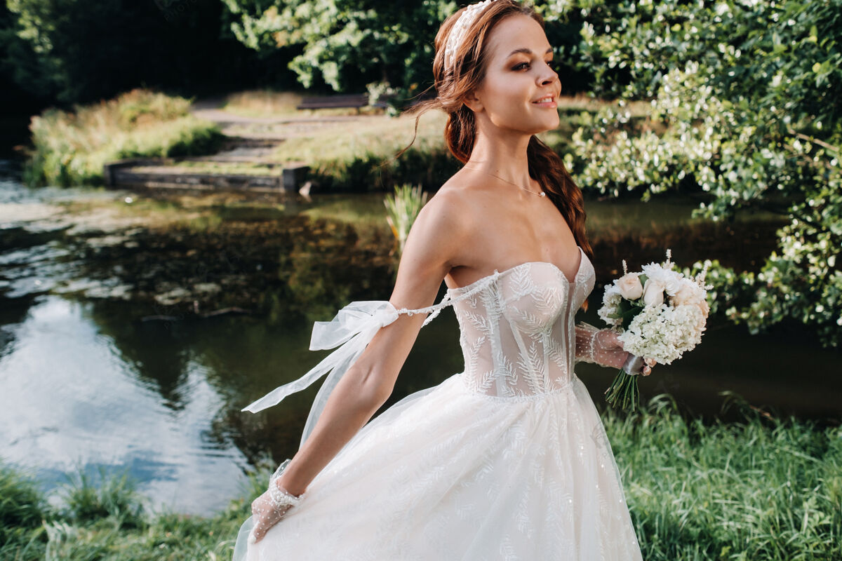 风景一个优雅的新娘在一个自然公园里穿着白色的裙子和一束花束的肖像浪漫新娘自由