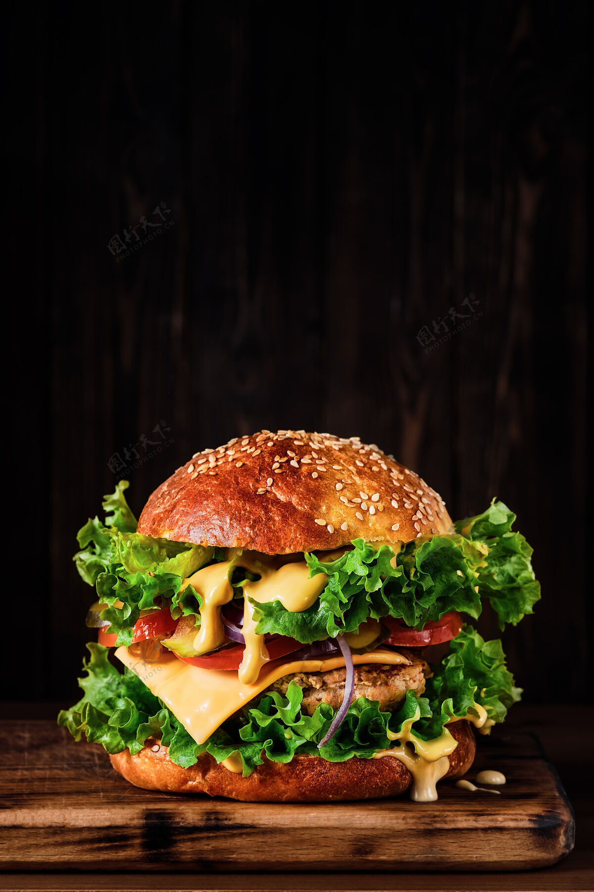 芝麻新鲜美味的烤制自制汉堡包 配火鸡肉片 奶酪 奶酪沙司和蔬菜 放在木板上 放在深色的烤盘上墙关闭向上 用复制空间选择焦点午餐肉西红柿