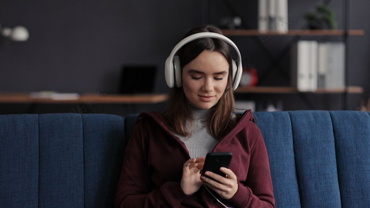 女人戴着耳机微笑的年轻女孩的肖像 在移动应用程序中选择喜爱的音乐曲目耳机房子室内