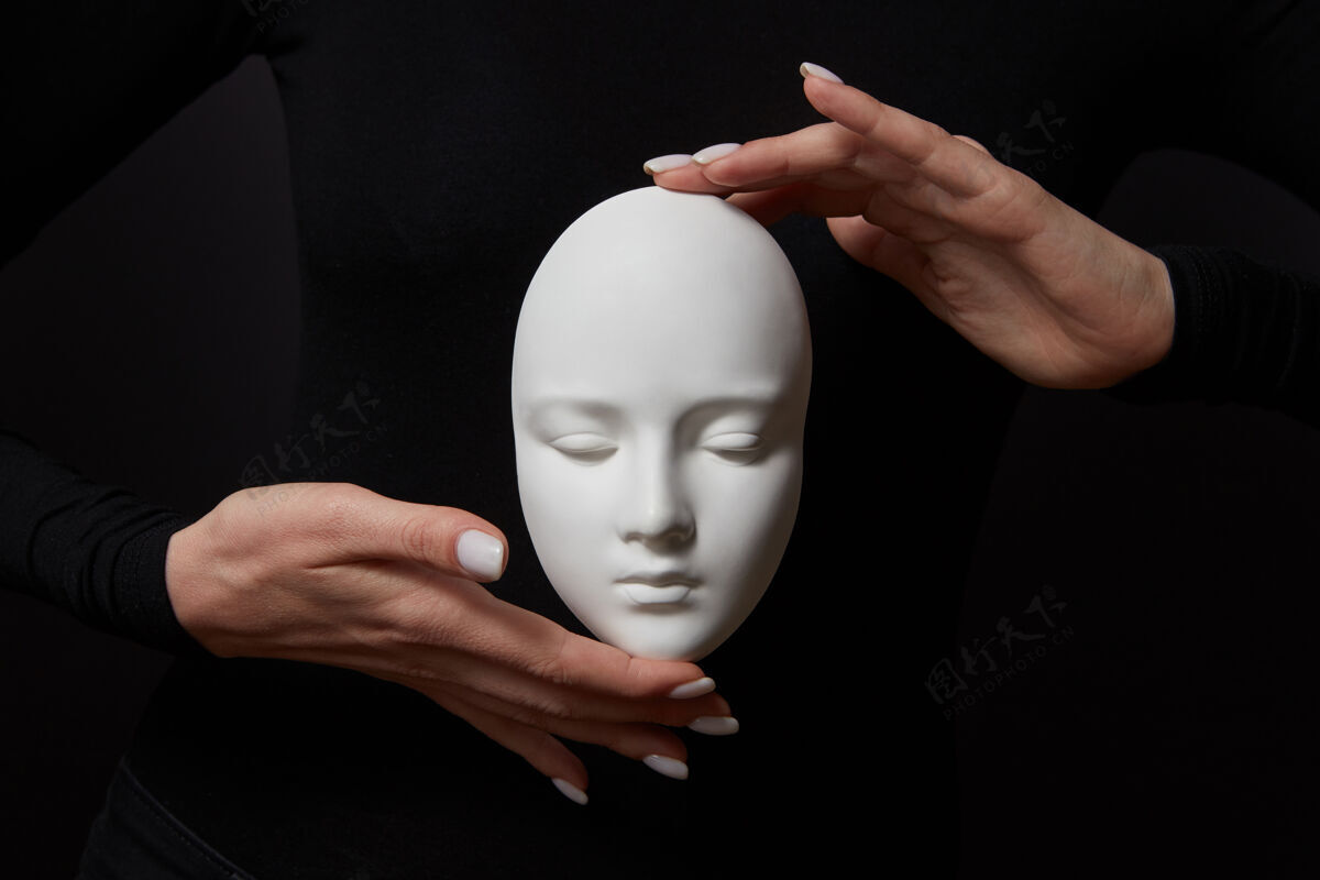 伪装白色的石膏面具脸上是拿着女人的手指在黑色的墙上 复制空间概念社会心理面具现代隐藏手指