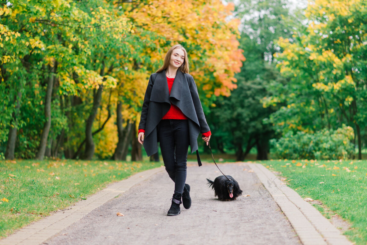 肖像秋天公园里日出时分 一位年轻迷人的女士抱着她的腊肠狗在户外团结微笑宠物