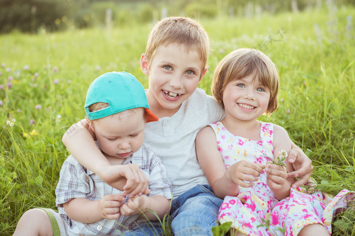 一起快乐的孩子们坐在外面绿色的草地上拥抱伙伴草花园