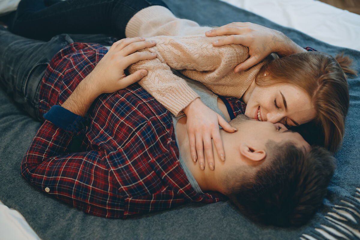 性感俯视图：一对迷人的年轻夫妇在床上面对面地拥抱 在接吻前笑着 而女孩在抚摸她的男朋友的脸室内浪漫吻