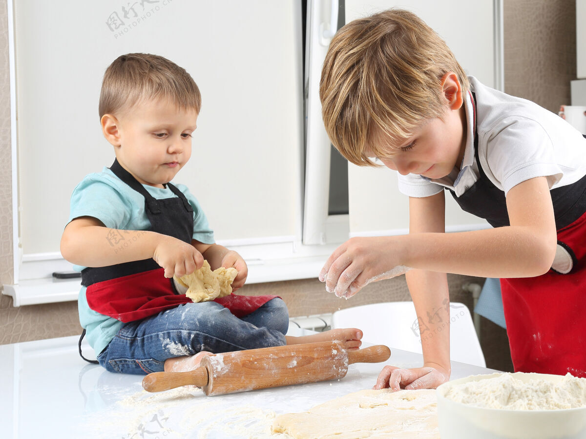 教学两个小男孩在厨房桌子上揉面团团队合作面粉儿子
