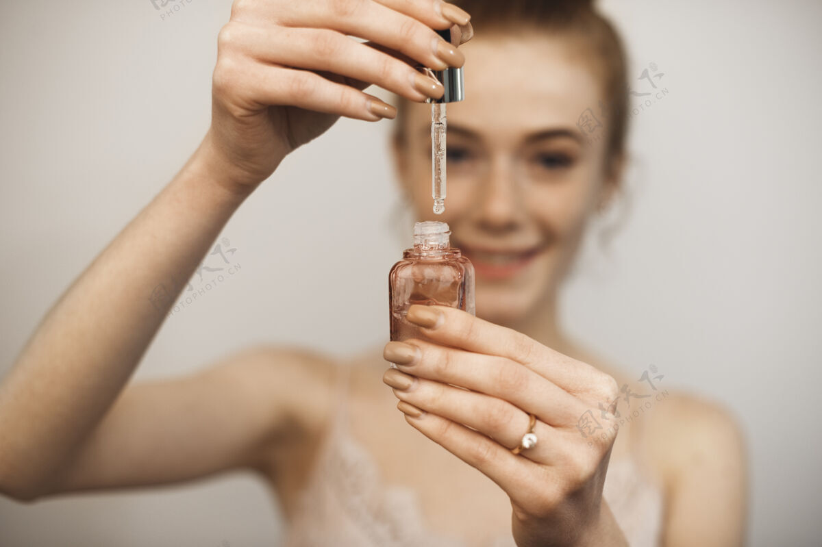 维生素一个年轻女子拿着滴管和一瓶透明质酸在一堵白色的墙前清除保湿药品