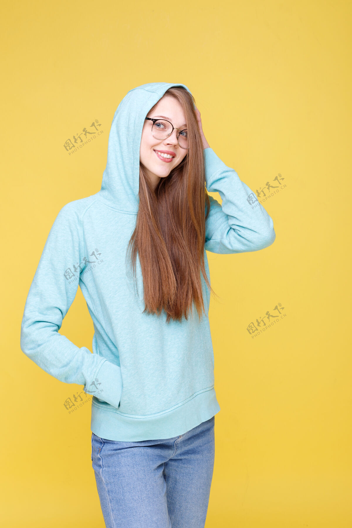 时尚迷人的女孩微笑与蓝色连帽衫与帽子在黄色的背景连帽衫搞笑毛衣