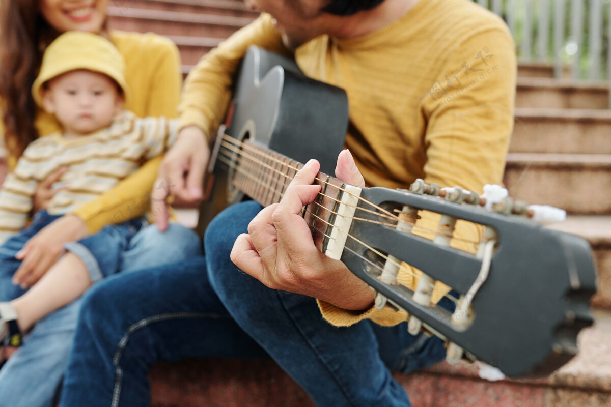 户外特写图片的年轻人弹吉他 他的可爱的小儿子 选择性的重点音乐家吉他休闲服