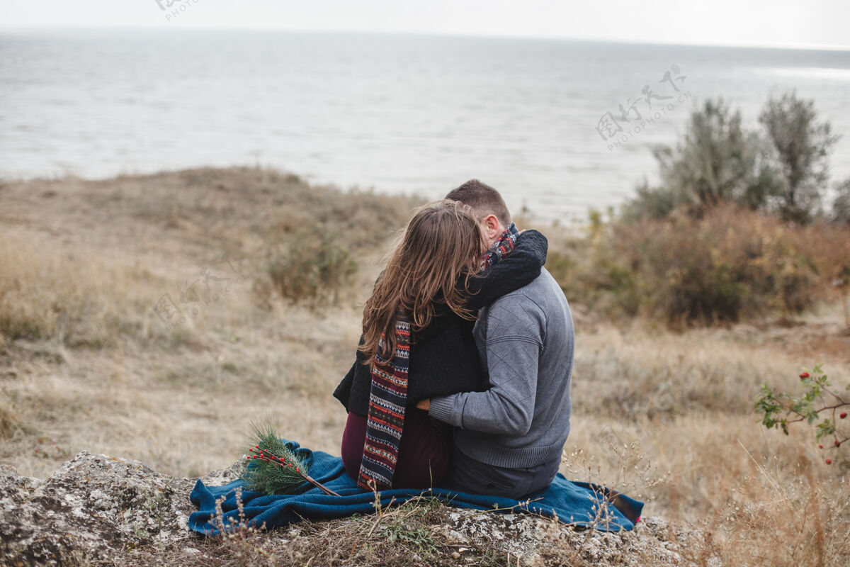 坐着拥抱坐在海滩岩石上的年轻夫妇年轻人户外