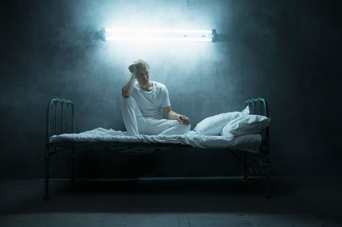 表情精神病患者坐在床上 黑暗的房间里…迷幻的人每晚都有问题 抑郁和压力 悲伤 精神病院人年轻家伙