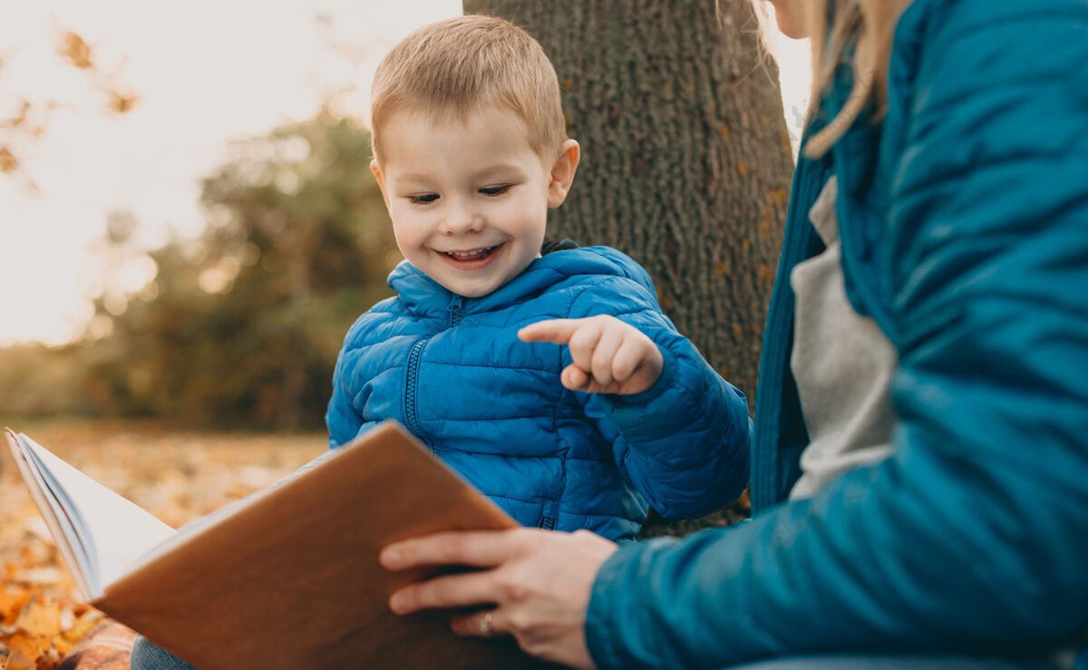 男人一个可爱的小男孩在户外看书的画像 他的妈妈微笑着文学学习学习