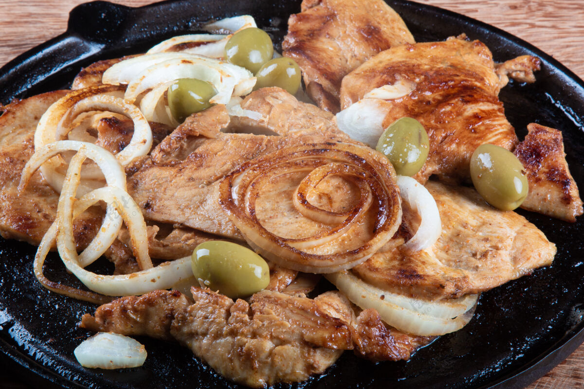 美味铁板上放着洋葱和橄榄的烤鸡鱼片烹饪家禽