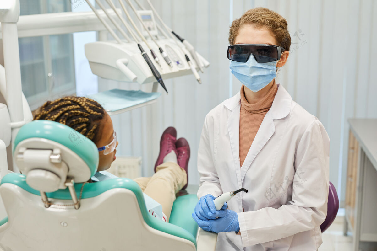 牙科健康戴着护目镜和面罩在牙科诊所治疗病人牙齿的年轻牙医的肖像护理患者技术
