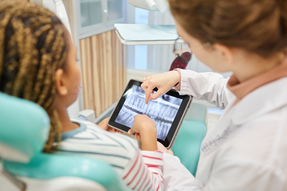 患者牙科诊所的病人和医生检查数字平板电脑上的x射线图像的后视图展示看体检