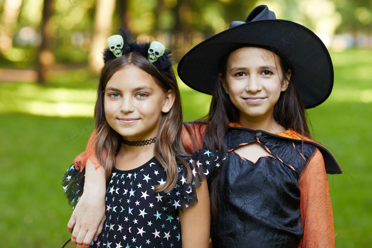 孩子两个穿着万圣节服装的女孩站在户外对着镜头微笑的画像青少年帽子打扮