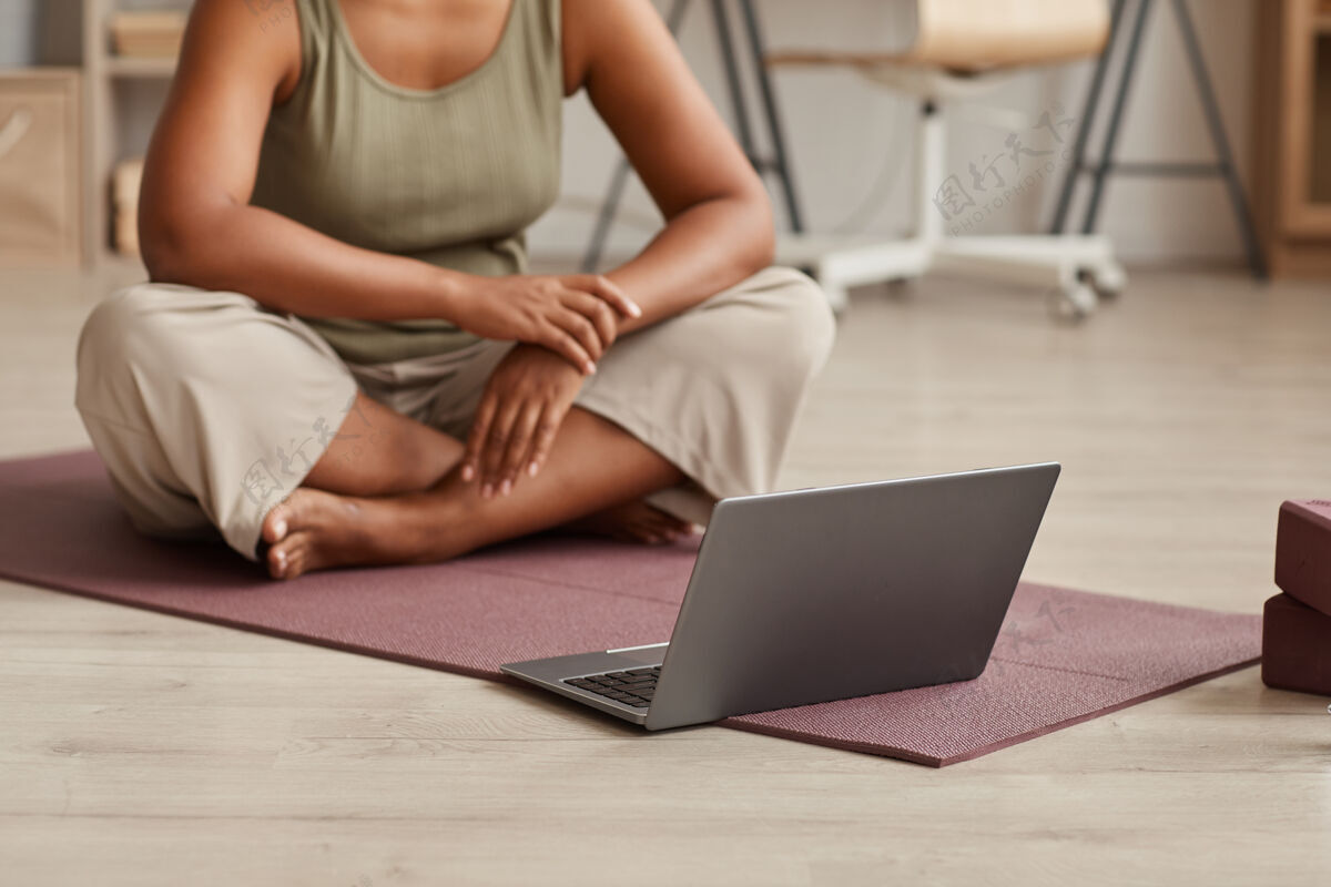 放松坐在笔记本电脑前的运动垫上 在家里在线观看瑜伽练习的女性特写镜头笔记本电脑舒适客厅