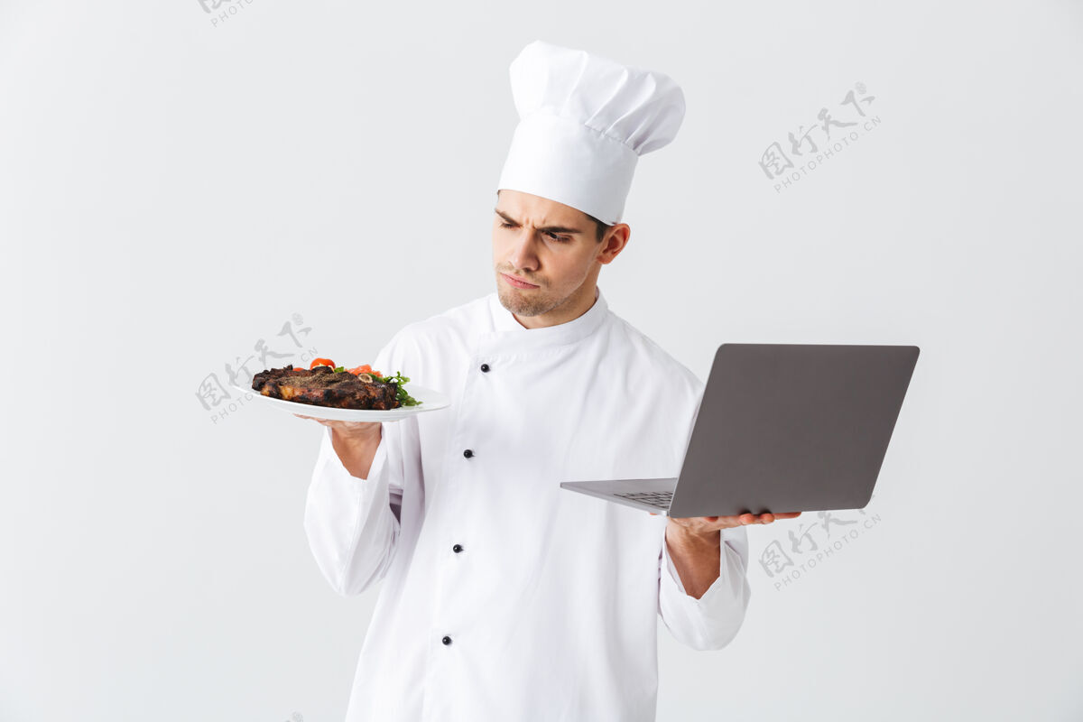 厨师正经的厨师穿着制服站在白色的墙上 拿着笔记本电脑 展示着一道菜盘子年轻人沟通