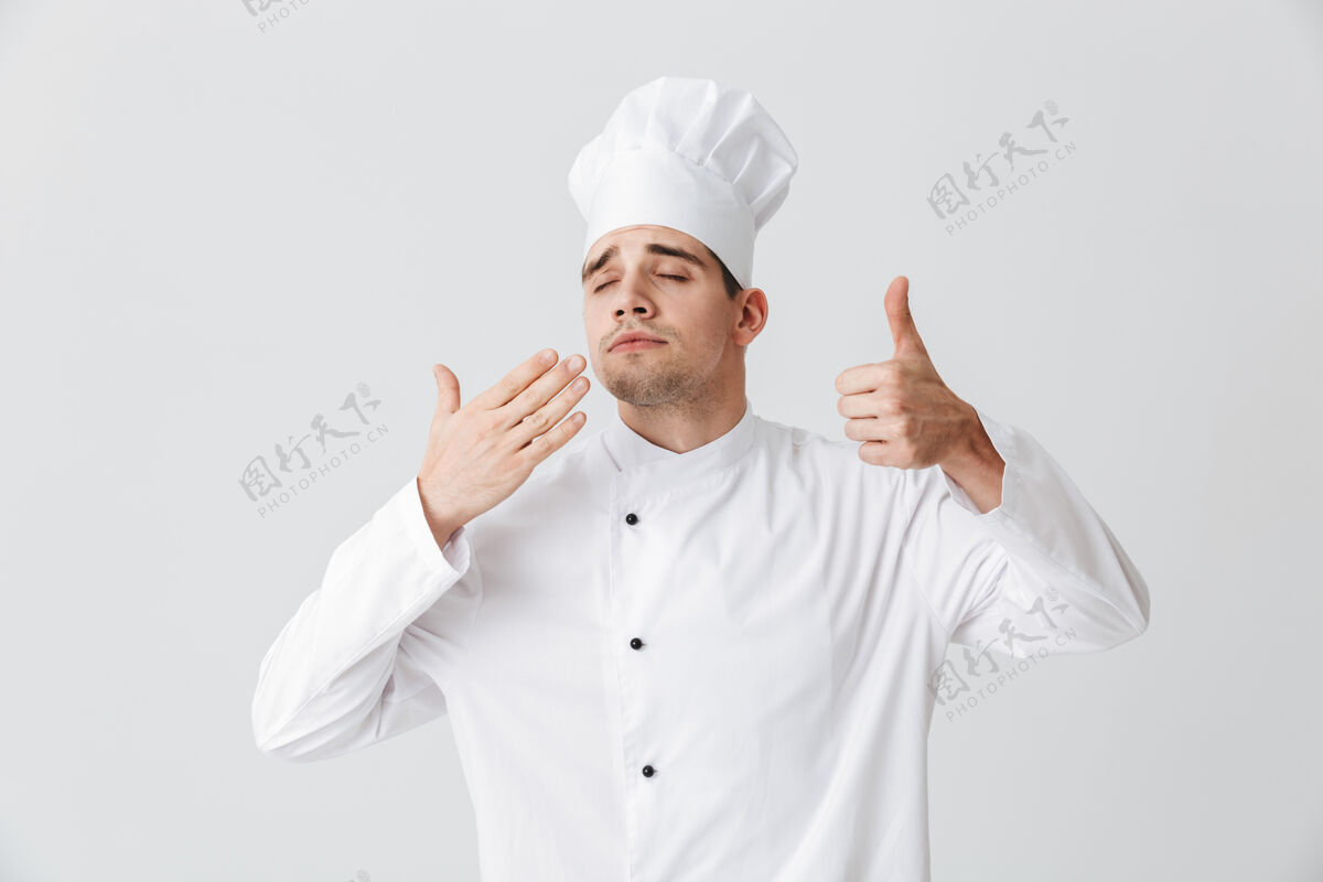 自信开朗的厨师穿着制服品尝着隔着白墙的味道烹饪工作气味