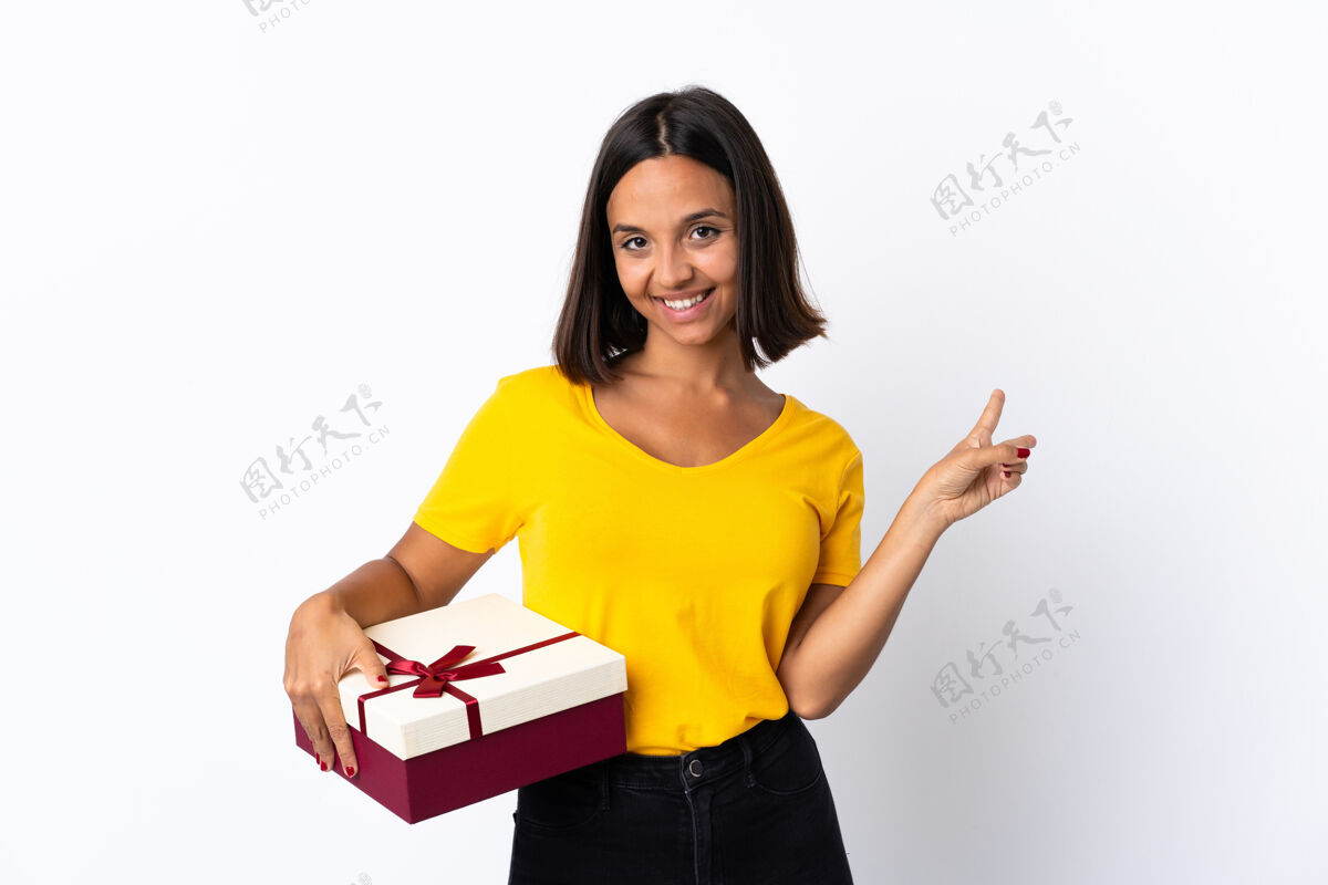 礼物年轻的拉丁女子手持礼物 面带微笑 并显示胜利的迹象成功包装聚会