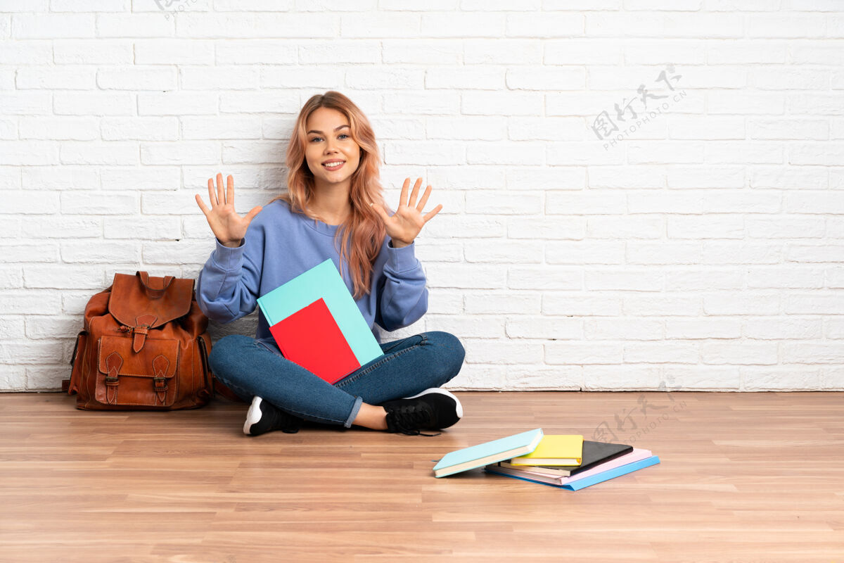 学生粉红色头发的女学生坐在室内的地板上用手指数到十学院学习全长