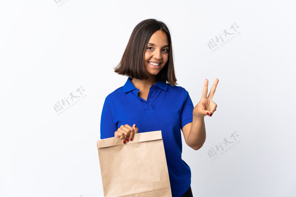 混合一个年轻的拉丁女人拿着一个杂货店的购物袋 脸上露出白色的微笑和胜利的标志成人黑发购物
