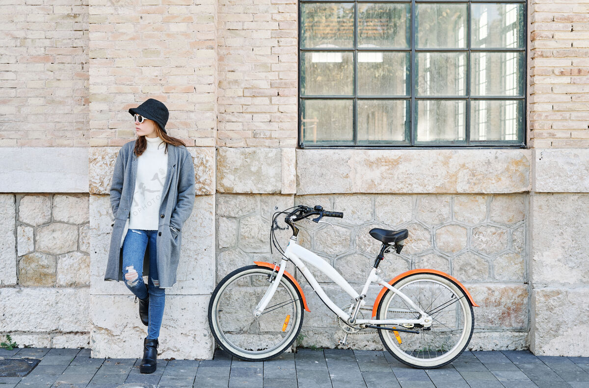 户外一个年轻漂亮的白人女孩的肖像 靠在墙上骑着自行车在城市里城市街道复古