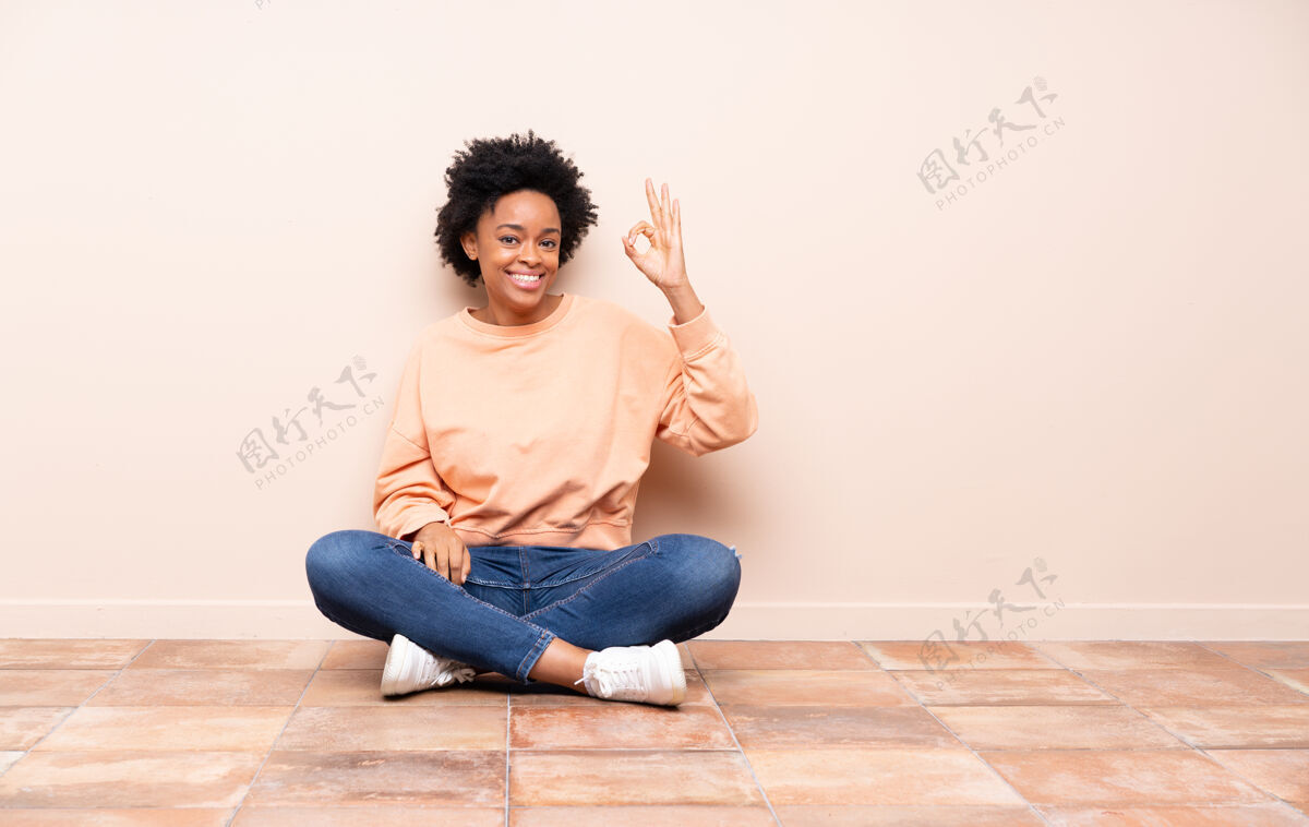 座位坐在地板上的非洲裔美国妇女用手指显示“ok”标志房间身体成人