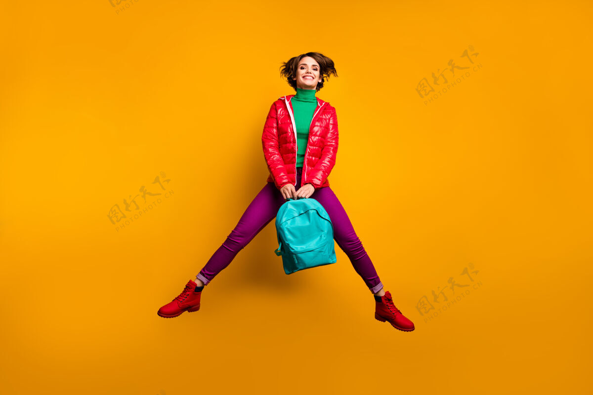 教育全尺寸照片欢快时髦有趣的青年学者女孩跳拿蓝色背包享受情感穿紫绿色裤子红色靴子学习积极高