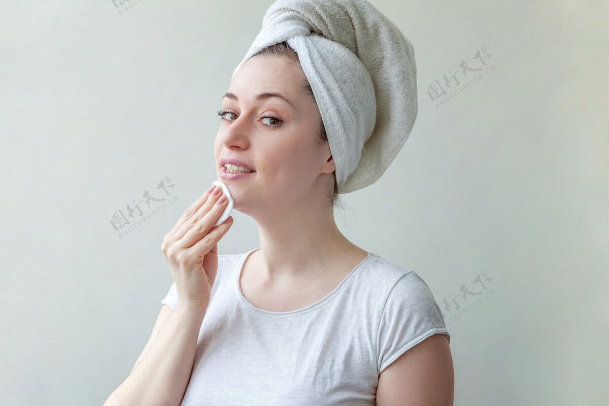 敏感头上戴着毛巾的微笑女人的美丽肖像 柔软健康的皮肤 用隔离在白色背景上的化妆棉卸妆水疗完美皮肤护理