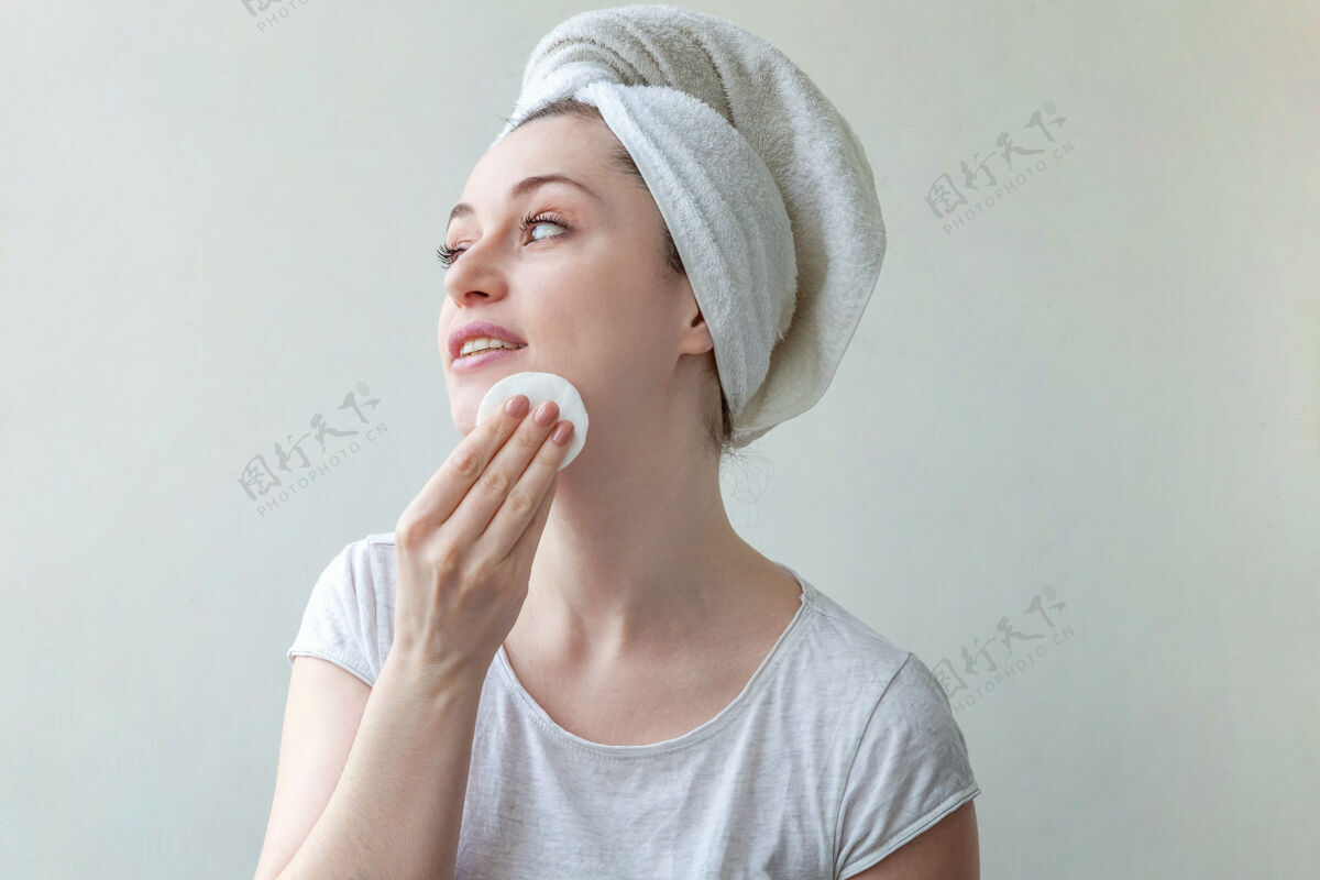 保健头上戴着毛巾的微笑女人的美丽肖像 柔软健康的皮肤 用隔离在白色背景上的化妆棉卸妆化妆品新鲜白色背景