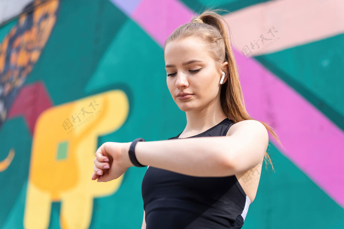 女性年轻的金发女子在户外训练时穿着运动服 戴着她的健身手镯 五颜六色的背景身体温暖运动