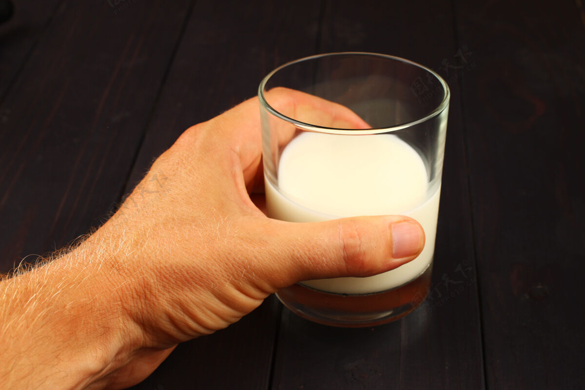 阴影手里拿着一杯牛奶放在黑暗的表面上罐子满的新鲜