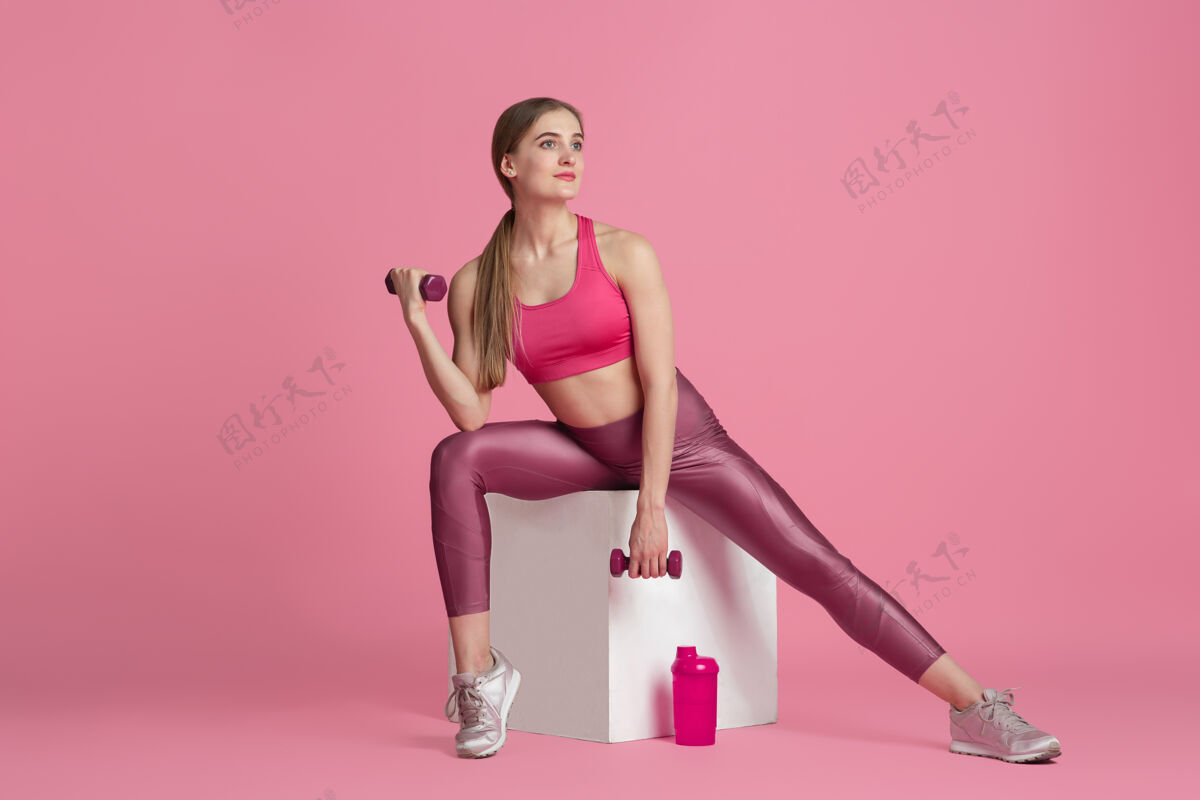 身体美丽的年轻女运动员在粉色工作室墙上练习单色肖像粉色女人健身